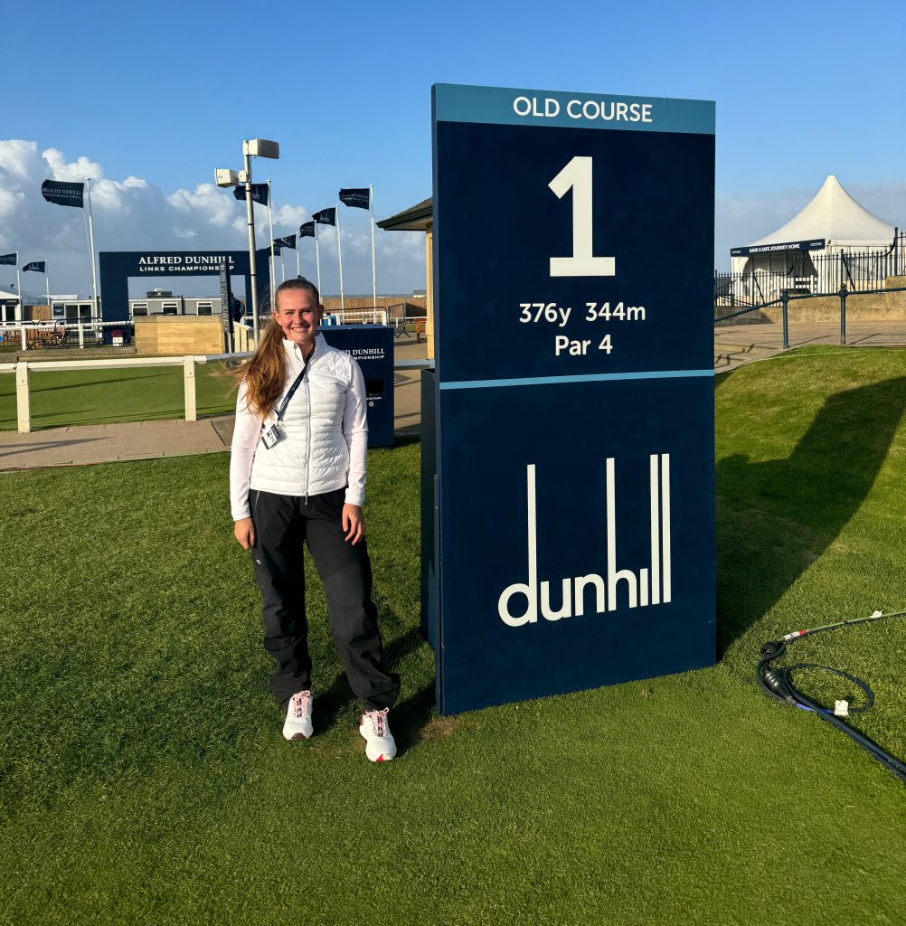 A woman (Georgina) stood in front of the Dunhill Links 1st hole tee box at The Old Course, St Andrews