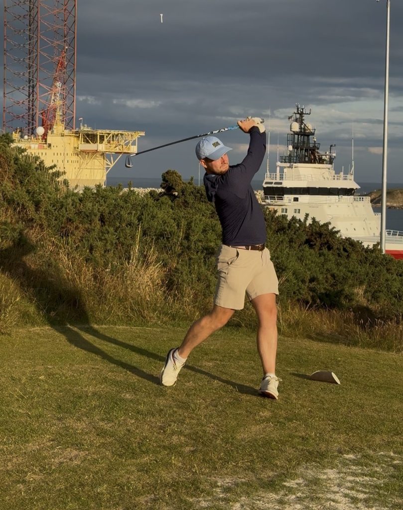 a golfer (Cameron) hitting a tee shot in front of ships at Balnagask Golf Course in Aberdeen