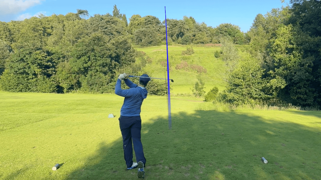 Cameron hits his tee shot on the 15th hole of Dalmuir Golf Course, a short par 3, with a blue tracer showing the trajectory of his golf ball.