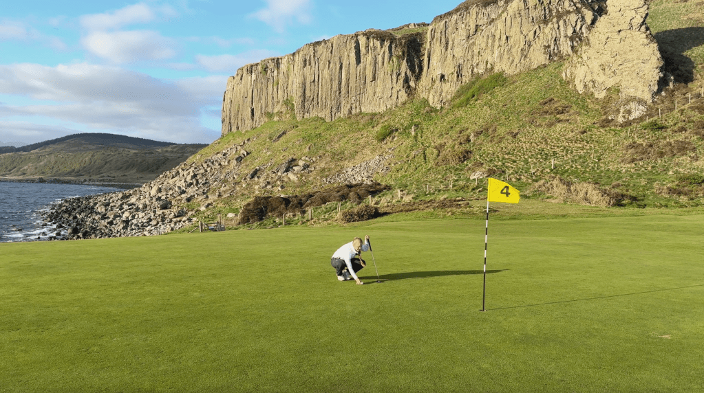 Georgina lines up a putt in front of a '4th' hole golf pin, on Shikine, Arran.